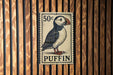 A 50 cent postage stamp featuring a puffin bird is displayed on a wooden wall.