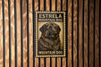 A metal sign with a dog image and text, mounted on a wooden wall.