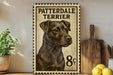 A framed poster of a patterdale terrier dog, with a price of 8 pence, is displayed on a shelf next to a wooden cutting board and some lemons.