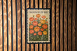 A vintage-style postage stamp featuring a floral illustration of Ranunculus flowers, which is affixed to a wooden wall.