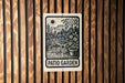 A sign for a patio garden is displayed on a wooden wall.