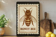 a framed illustration of a bee, specifically a honey bee, on a shelf.