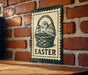 A green and white sign with a basket of Easter eggs is displayed on a brick wall.