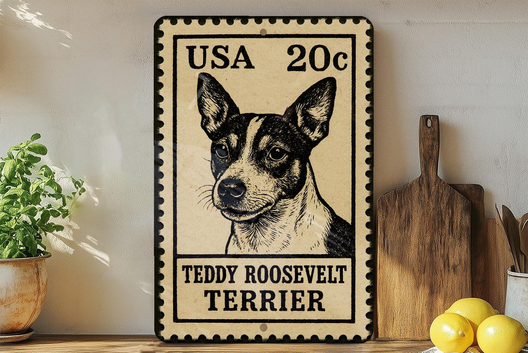 A vintage-style metal sign featuring a black and white illustration of a Teddy Roosevelt Terrier dog, with the text "USA 20c" and "Teddy Roosevelt Terrier" printed on it. The sign is displayed on a wooden shelf, with a potted plant and a wooden cutting board visible in the background.