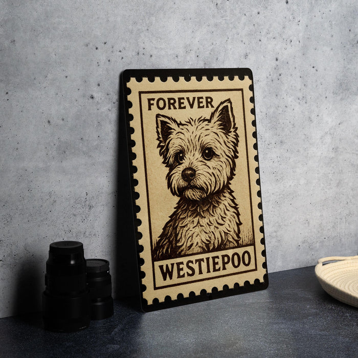 A framed poster of a Westie poo dog, with the text "Forever Westie poo" on it, is displayed on a countertop next to some black camera lenses.