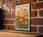 A framed illustration of a bed of orange and yellow flowers is displayed on a brick wall.