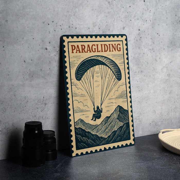 A framed poster of a paraglider is displayed on a table, with a stack of black camera lenses and a white plate nearby.