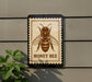 a honey bee on a postage stamp-like frame, mounted on a wall.