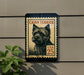 A Cairn Terrier dog stamp is displayed on a wall, with a plant to the left.
