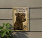 A postage stamp featuring a black and brown dog, specifically a Patteredale Terrier, mounted on a wall.