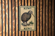 A metal sign featuring a kiwi bird illustration is mounted on a wooden wall.