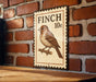 A metal sign with a bird illustration is mounted on a brick wall.