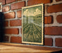 a framed illustration of a countryside landscape, with a brick wall and wooden table in the foreground.