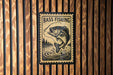 A sign with the text "BASS FISHING" and an illustration of a fish jumping out of the water, mounted on a wooden wall.