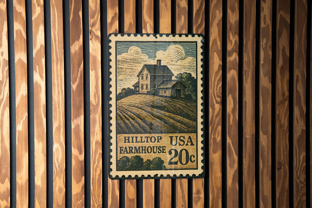 A vintage-style postage stamp featuring a farmhouse illustration, mounted on a wooden wall.