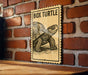 A wooden table with a wooden surface, and a framed poster of a box turtle is mounted on a brick wall.