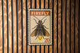 A framed image of a Firefly insect, with the text "FIREFLY" and the number "20" printed on it, is displayed on a wooden wall.