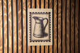 a wooden wall with a framed illustration of a pitcher, which appears to be a decorative piece or a sign.