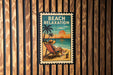 A beach relaxation sign with a person sitting in a beach chair and a palm tree in the background, set against a wooden wall.