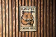 A metal stamp featuring a hamster eating a seed, mounted on a wooden wall.