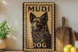 A wooden sign with a dog image and the text "MUDI DOG" on it, placed on a shelf next to a potted plant and some kitchen utensils.