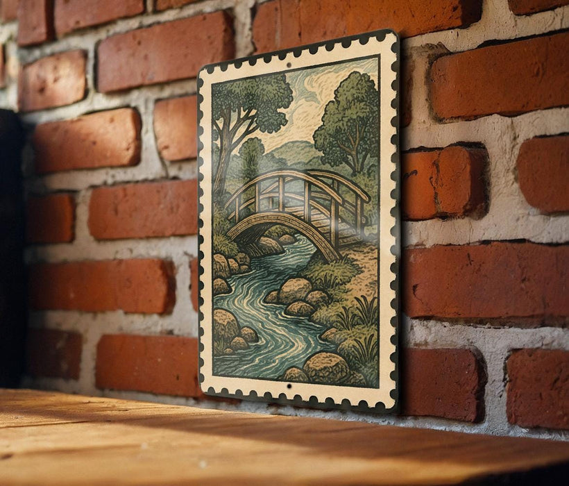 A framed illustration of a bridge over a river is hanging on a brick wall.