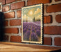 A framed image of a field of lavender flowers is displayed on a brick wall.
