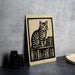 A metal sign featuring a black and white illustration of a cat sitting on a bookshelf, with various books surrounding it.