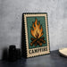 A metal sign with a campfire illustration on it, placed on a countertop next to some black camera lenses.