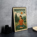 A metal stamp depicting a woman in a meditative pose, with a mountain landscape and a sun in the background.