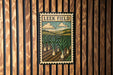 A framed illustration of a field with tall plants, likely representing a farm or agricultural landscape, is displayed on a wooden wall.