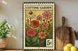 A vintage-style metal sign with a floral design, featuring a variety of colorful flowers and plants, is displayed on a shelf next to a wooden cutting board and some kitchen utensils.