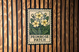 A vintage-style stamp-like sign with a floral design and the text "PRIMROSE PATCH" is displayed on a wooden wall.