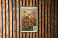 A vintage-style stamp depicting a garden scene with flowers and plants, mounted on a wooden wall.