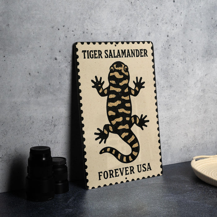 A metal sign with a tiger salamander illustration and the text "TIGER SALAMANDER FOREVER USA" on it, placed on a table next to some black camera lenses.