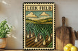 a framed illustration of a field with a variety of vegetables, including onions, placed on a shelf next to a wooden cutting board and a potted plant.