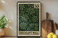 a framed print of a postage stamp with a design of green succulent plants, placed on a shelf next to a wooden cutting board and some lemons.