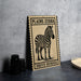 A framed image of a zebra is displayed on a table, with a stack of black camera lenses to the left and a woven basket to the right.