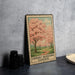 A vintage-style metal sign with a cherry blossom tree illustration, placed on a dark surface against a concrete wall.