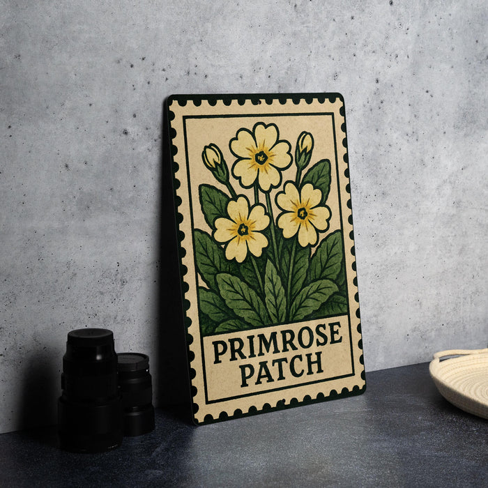 A framed print of a yellow flower with green leaves, labeled "Primrose Patch", is displayed on a table next to a stack of black camera lenses.