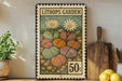 A vintage postage stamp featuring a colorful illustration of various cacti and flowers, with the text "LITHOPS GARDEN" and the denomination "50c". The stamp is displayed on a shelf next to a wooden cutting board and a potted plant.