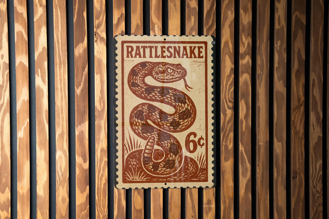A metal sign with a snake design is mounted on a wooden wall.