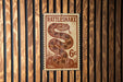 A metal sign with a snake design is mounted on a wooden wall.