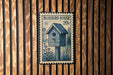 A postage stamp-like sign with a birdhouse illustration is mounted on a wooden wall.