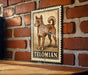 A metal sign with a drawing of a dog, mounted on a brick wall.