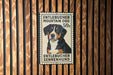 A metal sign with a picture of a dog, mounted on a wooden wall.