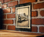A black and white illustration of a bench is displayed on a brick wall, mounted on a wooden surface.