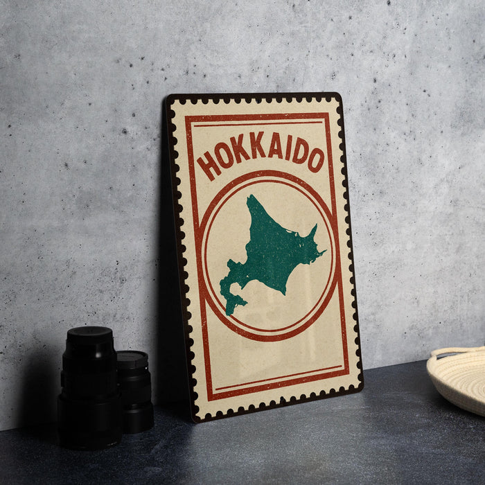 A vintage-style metal sign with the text "HOKKAIDO" and a map of Japan, placed on a dark surface next to some black camera lenses.