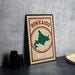 A vintage-style metal sign with the text "HOKKAIDO" and a map of Japan, placed on a dark surface next to some black camera lenses.