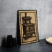 A framed illustration of an old-fashioned stove is displayed on a countertop, accompanied by a stack of black containers and a woven basket.